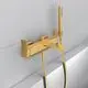 Brausearmatur in Brushed Gold von Ideal Standard, bestehend aus Mischbatterie, Handbrause, Schlauch und Wandhalter, montiert an einer wandähnlichen Oberfläche.